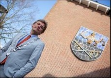 Man in een grijs pak kijkt omhoog naar een bakstenen gevel met een wapen