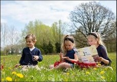 Drie kinderen lezen samen in een bloemenweide