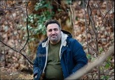 Portret van een man in een blauwe jas tussen kale bomen